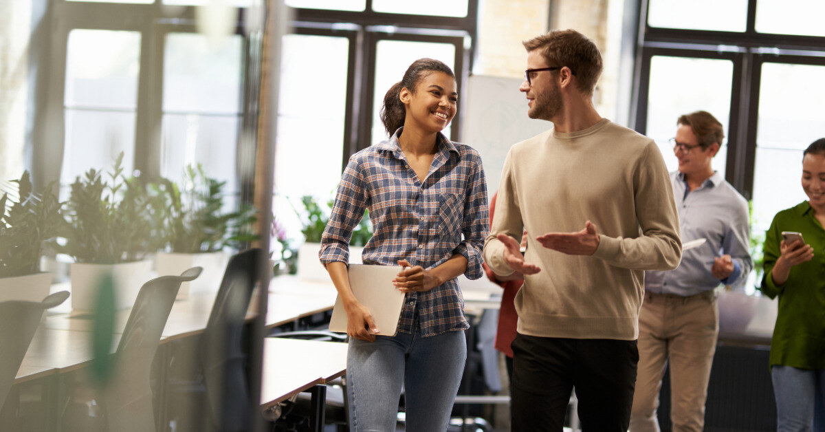 Two young diverse business people, male and female coworkers talking, discussing project and smiling while walking down the modern office. Informal conversation at work