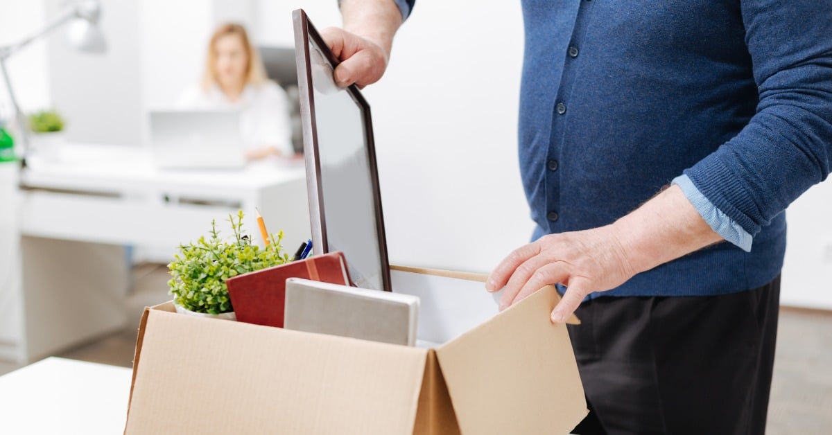 fired employee standing in the office and gathering box with personal stuff while holding the belongings